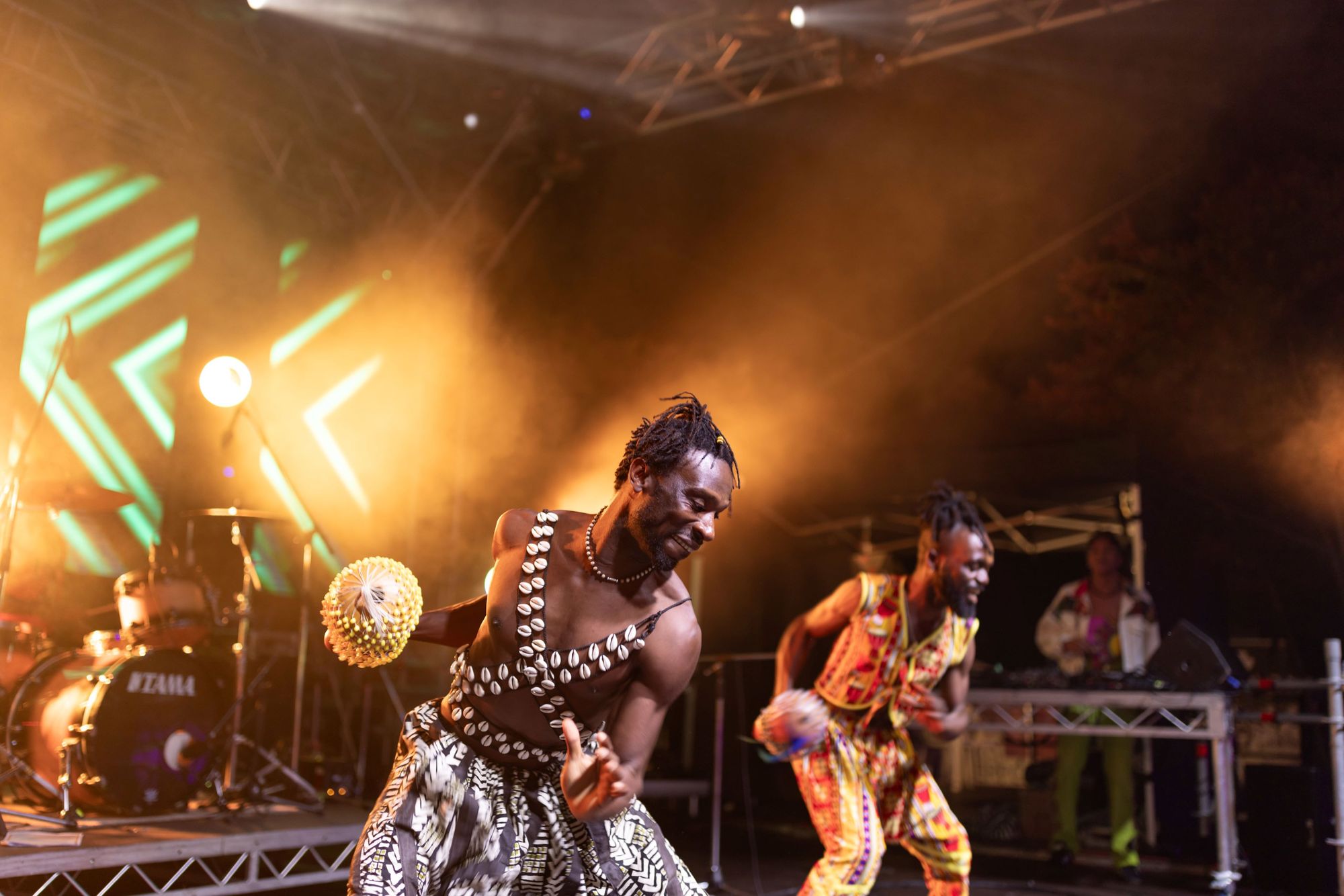 Two joyful male performers in traditional attire dancing energetically on a stage with glowing percussion instruments.