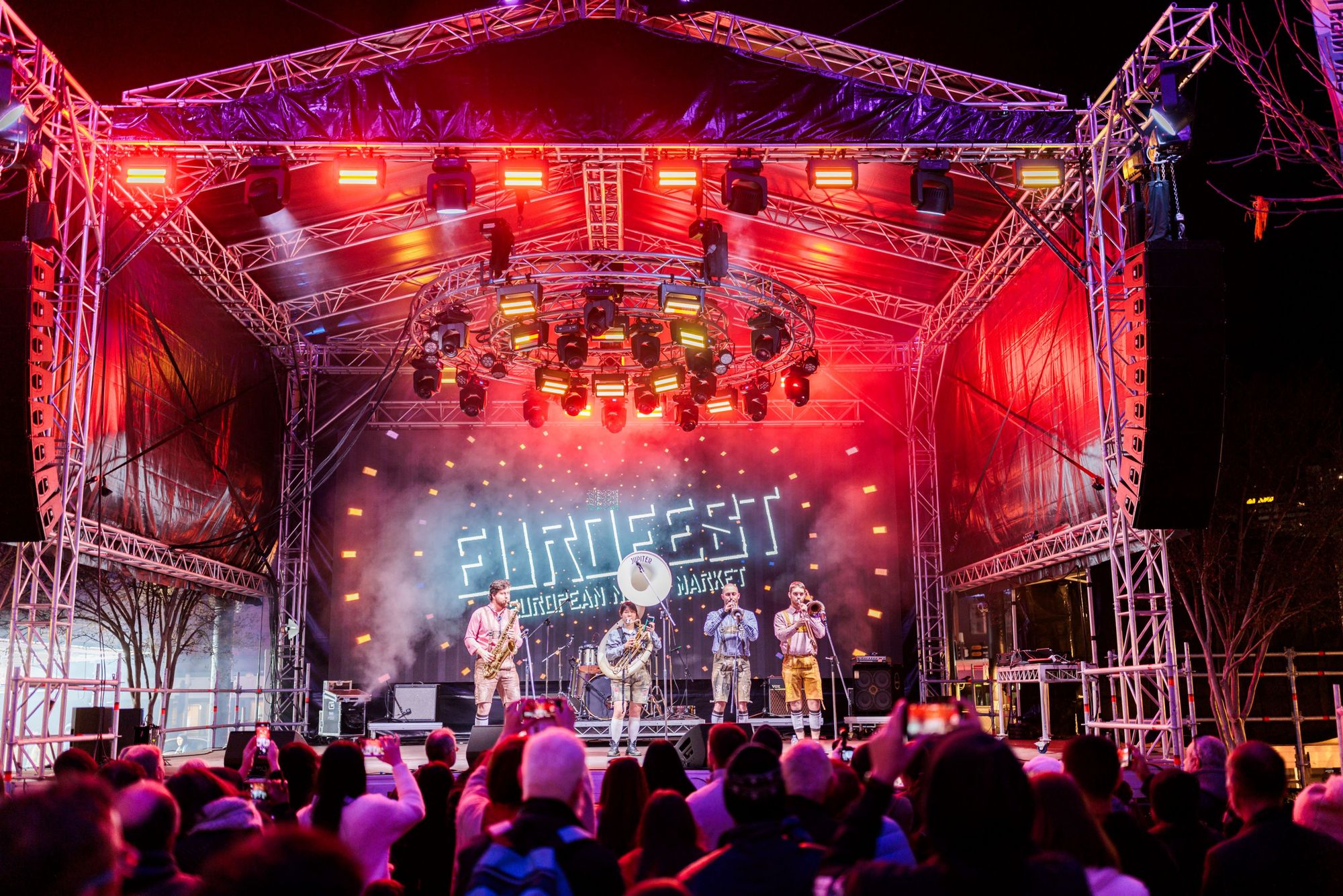 A band performing on a large outdoor stage lit with red and purple lights in front of a large crowd at Eurofest.