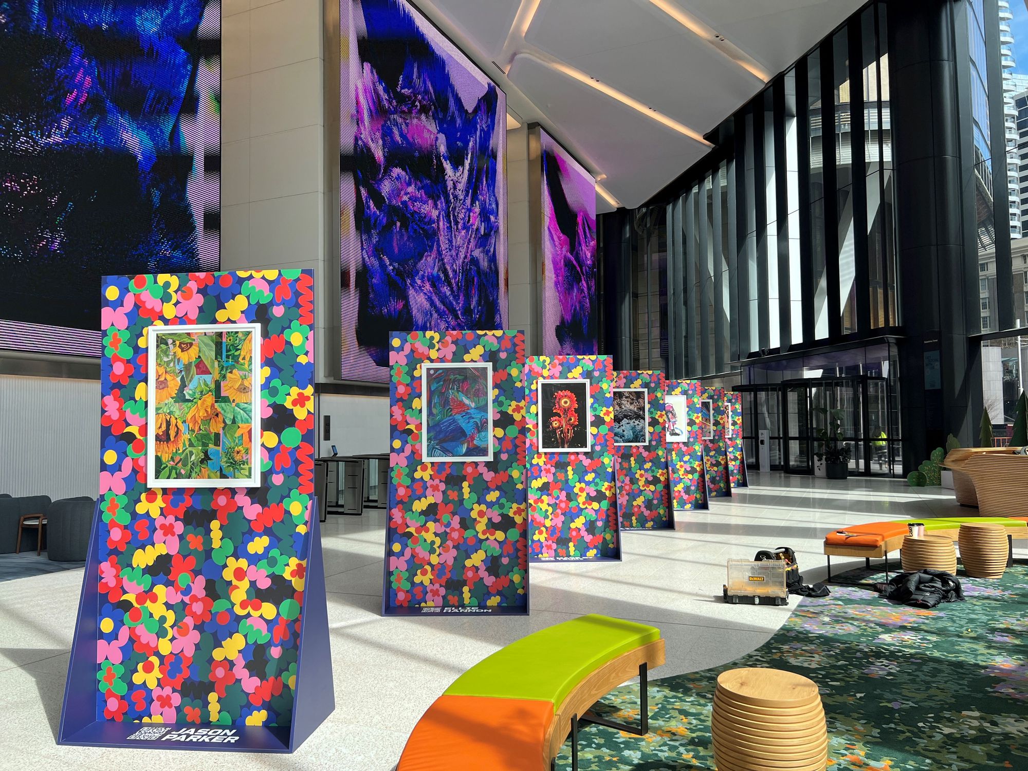 Colourful art exhibition in a modern building lobby, featuring vibrant floral-patterned displays and bright seating.