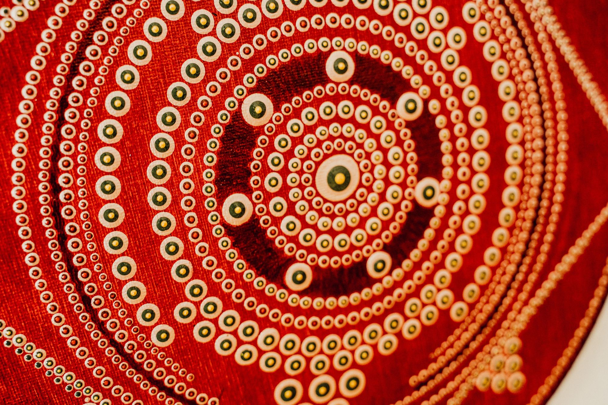 Abstract design of concentric circles with small dots on a red textured background, featuring earthy tones of white, brown, and green.
