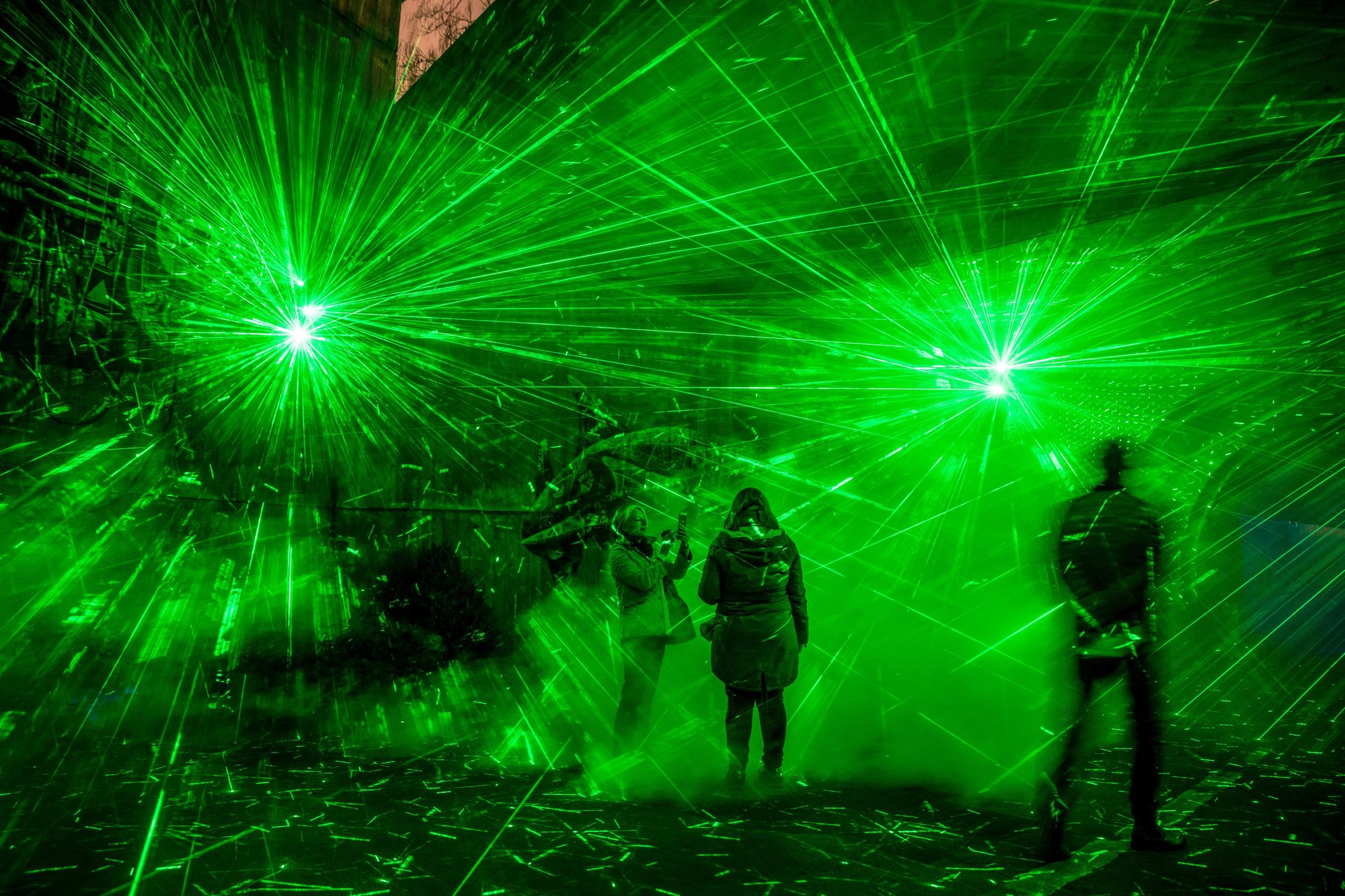 People take photos inside an immersive installation of green laser and fog