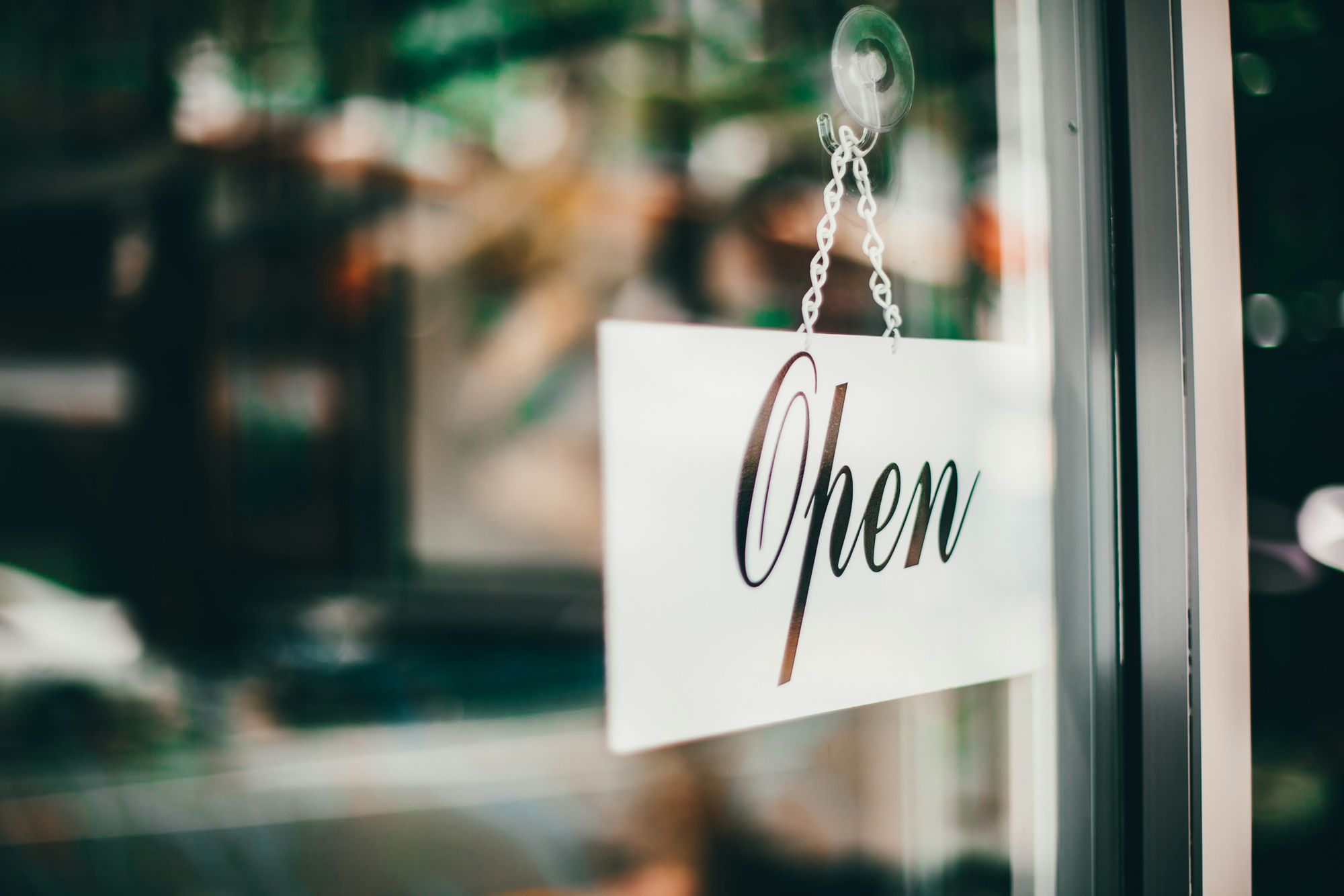 A white sign with the word "Open" hangs on a glass door, indicating that a store is ready for business.
