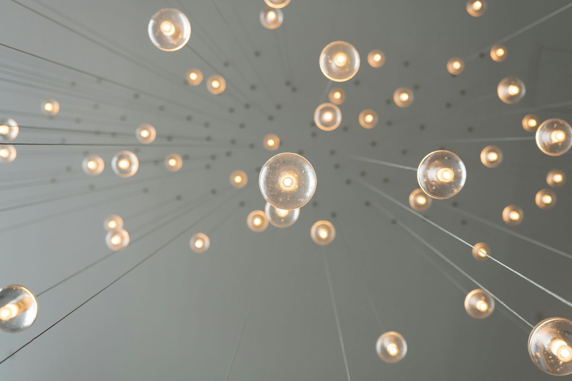 A cluster of hanging round light bulbs viewed from below, evenly spaced, creating a starry effect against a gray ceiling background.