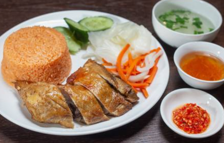 Plate with sliced roasted duck, orange rice, cucumber, cabbage, and pickled vegetables. Accompanied by soup, chili paste, and dipping sauce.
