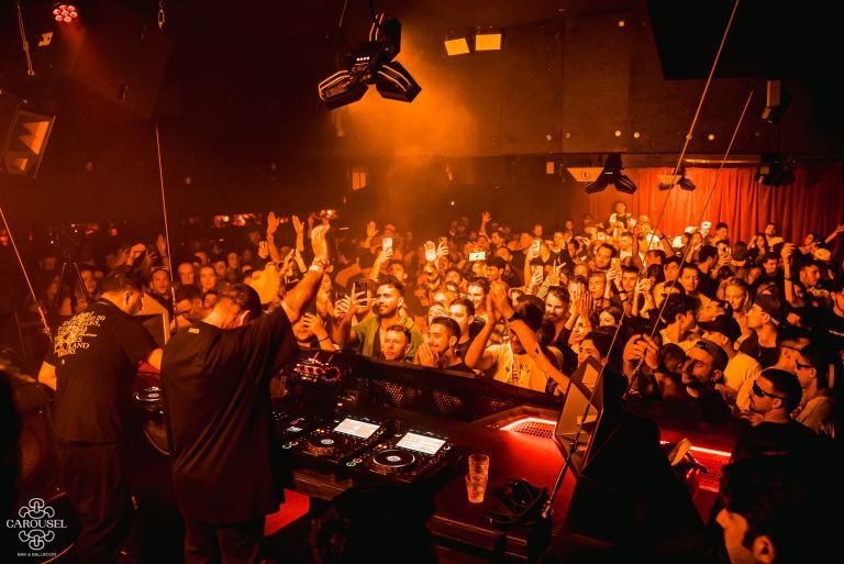 DJ performing in a dimly lit room to a large appreciative audience