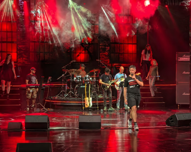 Band and performers rehearsing on a large red-lit stage aboard Mein Schiff during a live production rehearsal.