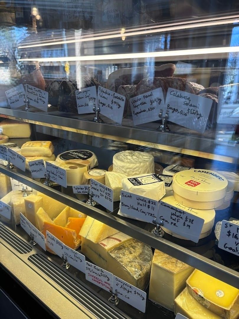 A refrigerated deli case filled with various cheeses, neatly labeled and priced, displayed under bright lighting.