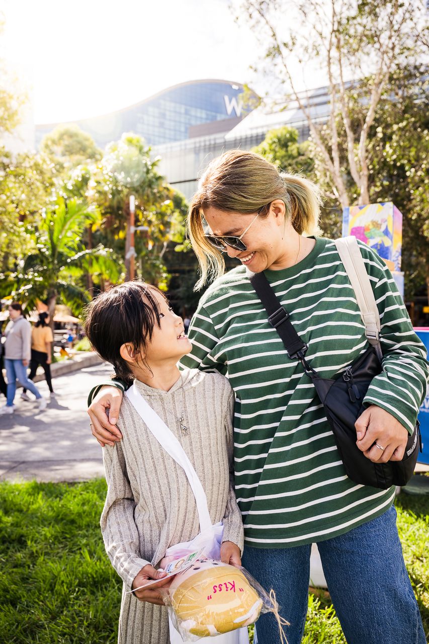 A mother and young daughter share a warm moment surrounded by colourful festival decorations at the Buddha’s Birthday event in Darling Harbour.