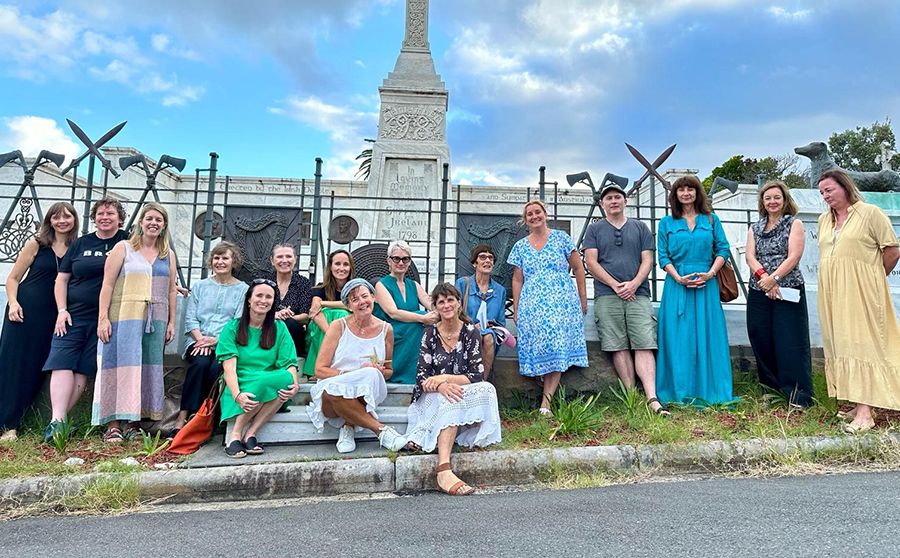 A group of people posing together in front of a historical monument with a cloudy sky in the background. Some are sitting, others standing.
