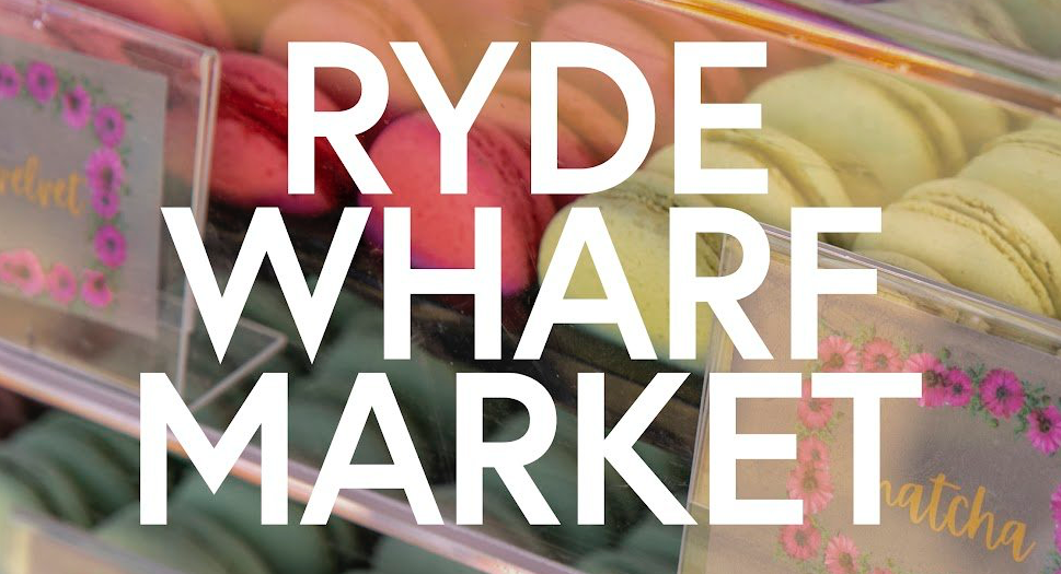 Text "RYDE WHARF MARKET" over colorful macarons in a display case with labeled compartments, featuring flavors like matcha.