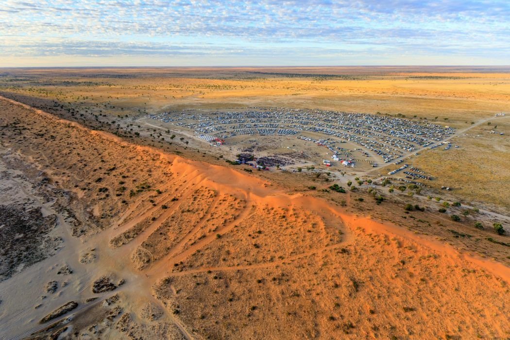 Big Red Bash: Campers set up at iconic outback music festival, red sand dunes in background under a blazing sun.