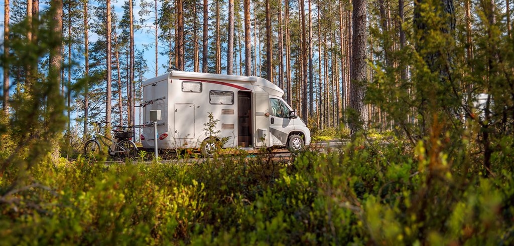 Autocaravana estacionada en camping con toldo abierto y sillas, ambiente vacacional.