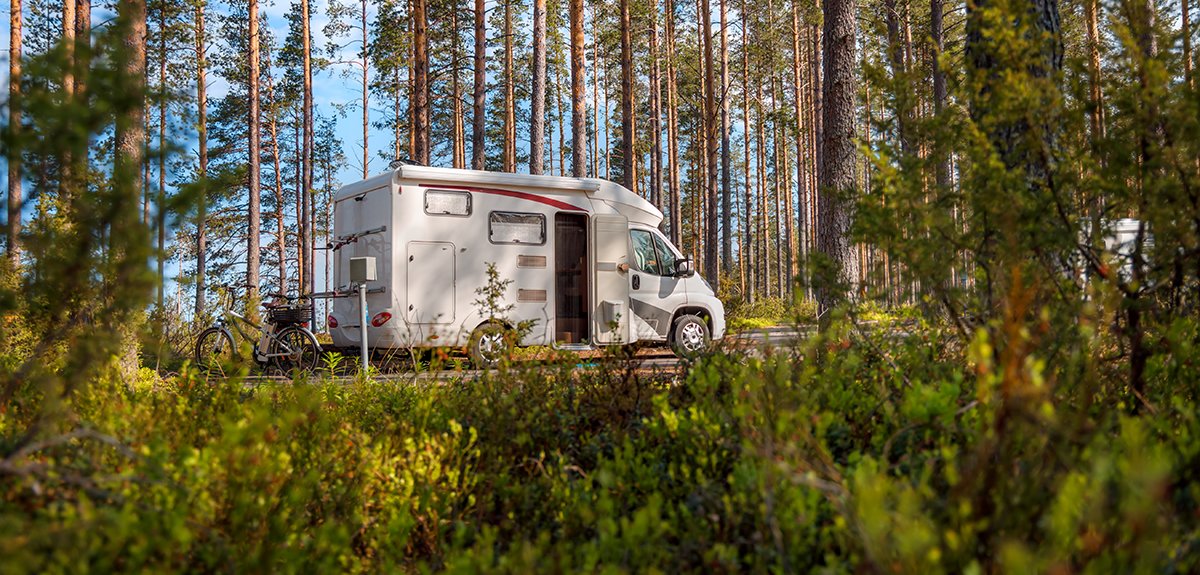 Autocaravana estacionada en camping con toldo abierto y sillas, ambiente vacacional.