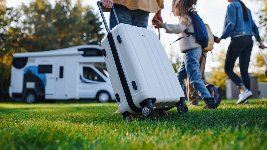Autocaravana familiar en camping con niños jugando y paisaje de montaña al fondo.