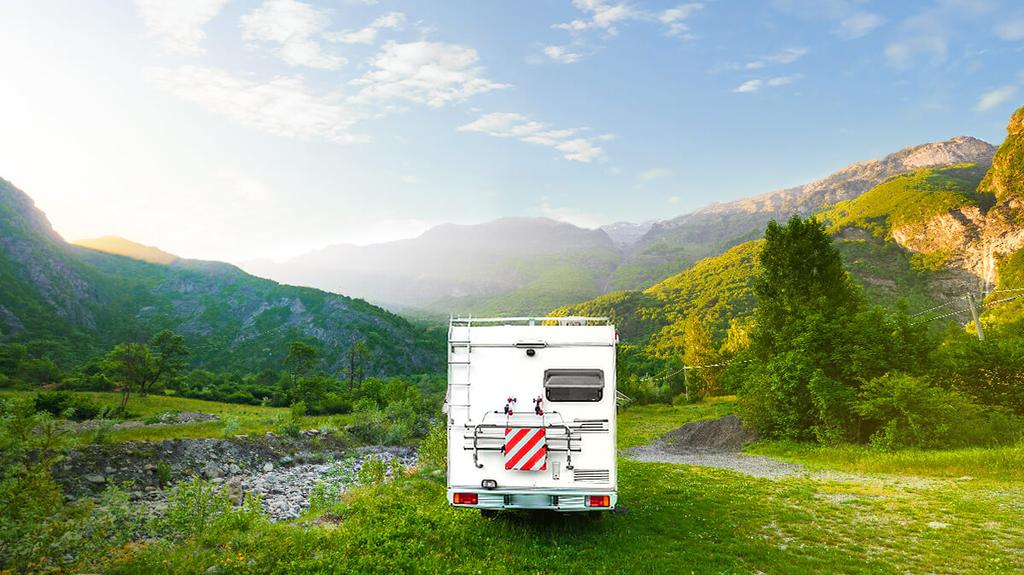 Autocaravana estacionada en la naturaleza con montañas al fondo. Viajar sostenible y aventura.