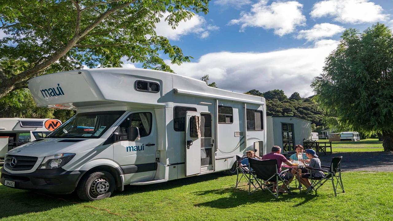 Family enjoying a BBQ at a North Island holiday park, with campervan parked nearby.