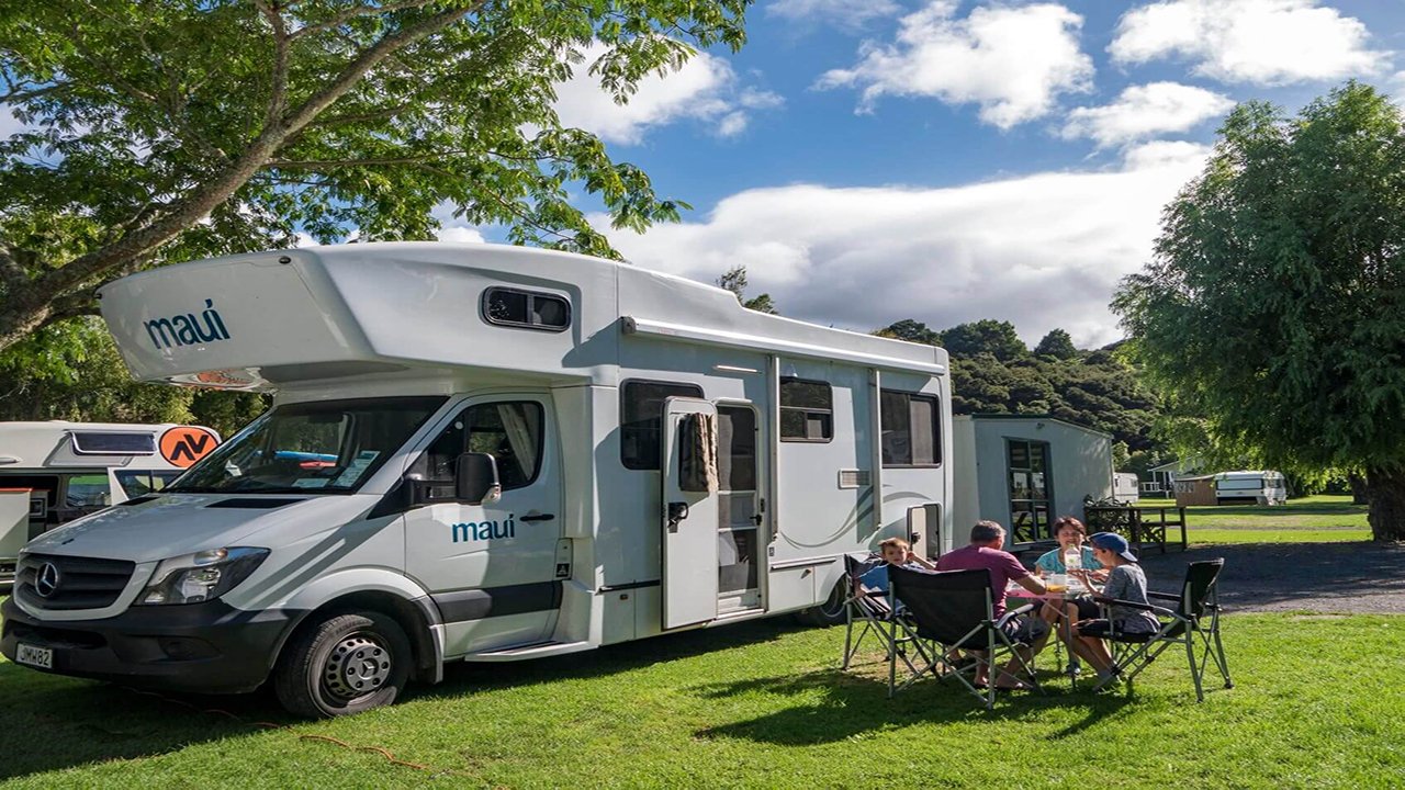 Family enjoying a BBQ at a North Island holiday park, with campervan parked nearby.