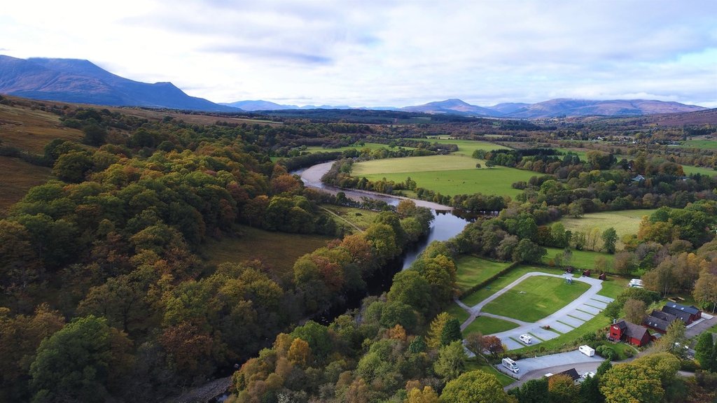 Campervan at a lochside campsite in the Highlands, with mountains reflected in the calm water.