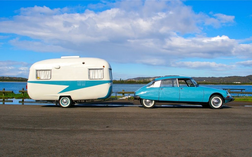 Caravana enganchada a coche viajando por carretera soleada. Vacaciones y aventura al aire libre.