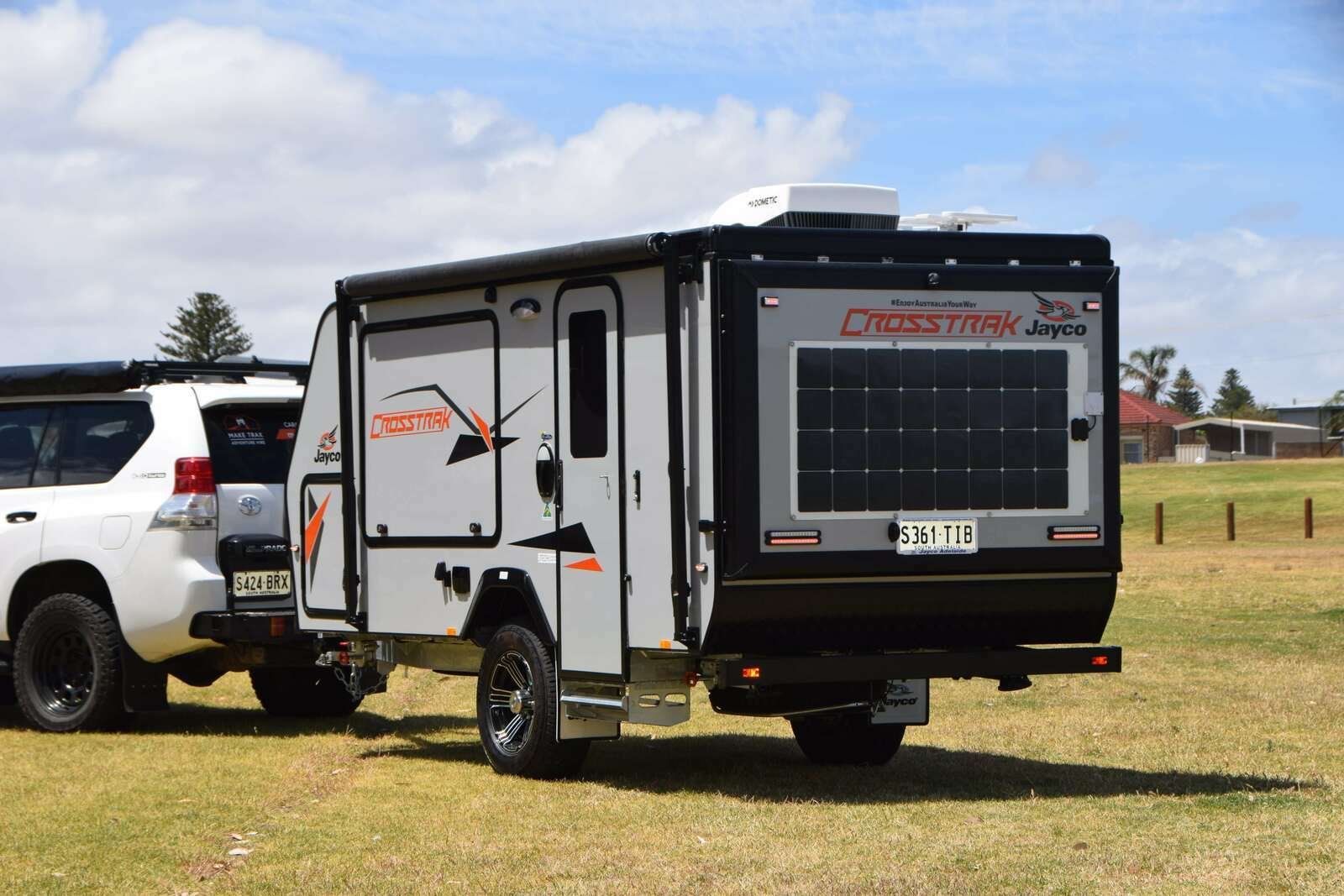 A Jayco Crosstrak camper trailer hired on Camplify attached to a white SUV, parked on grass under a partly cloudy sky.
