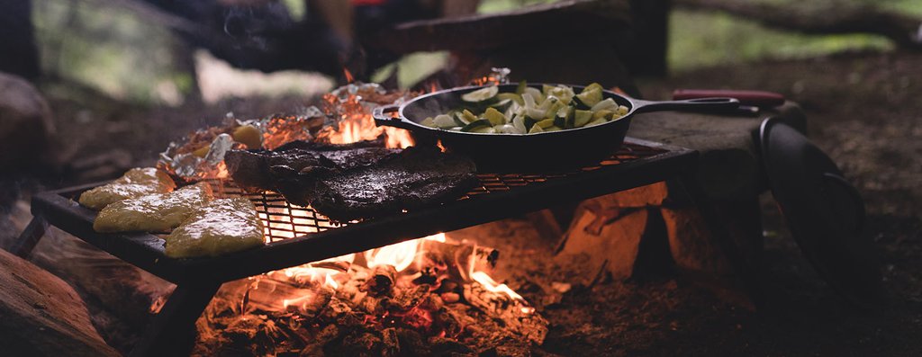 Campfire cooking scene with caravan in background. Holidaymakers enjoying outdoor meal.