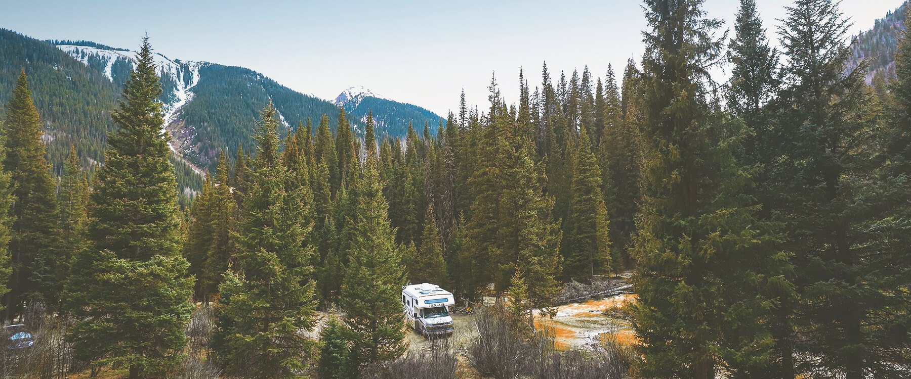 Autocaravana moderna en ruta por carretera soleada con paisaje de montañas al fondo.
