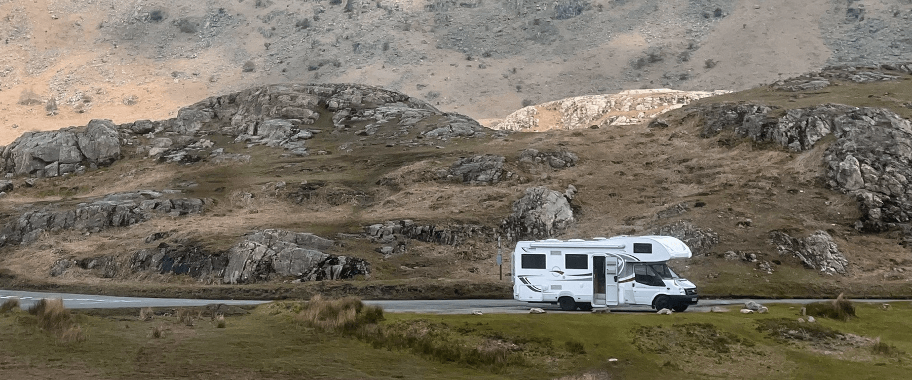 Campervan parked up on scenic coastal road, blue sea and sky backdrop.