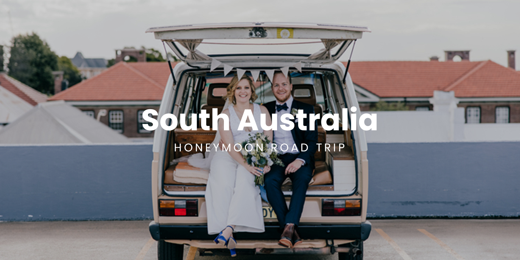 Couple toasting wine glasses in front of a campervan, South Australian vineyard in background.