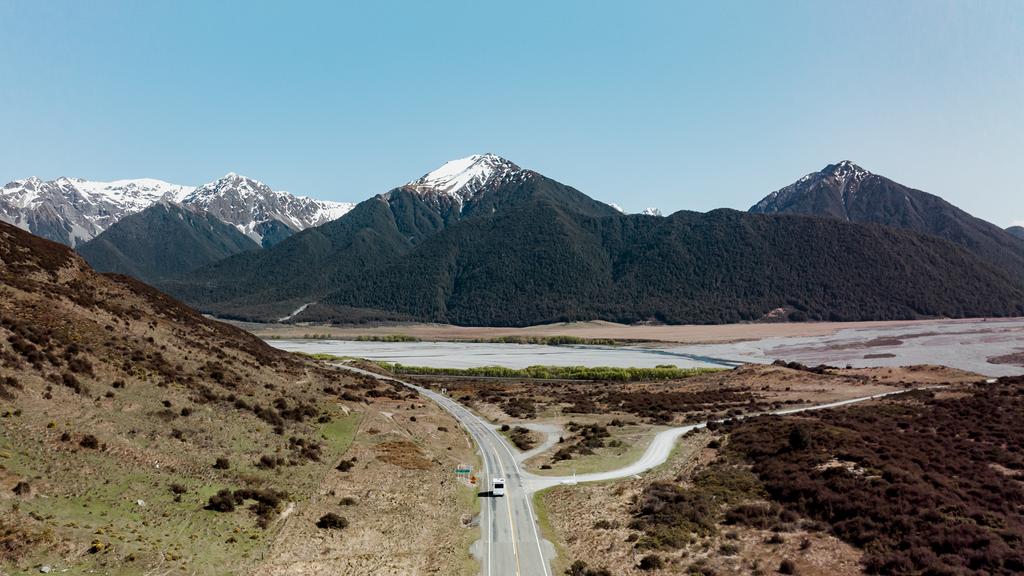 Campervan overlooking a turquoise lake and snow-capped mountains, South Island, NZ.