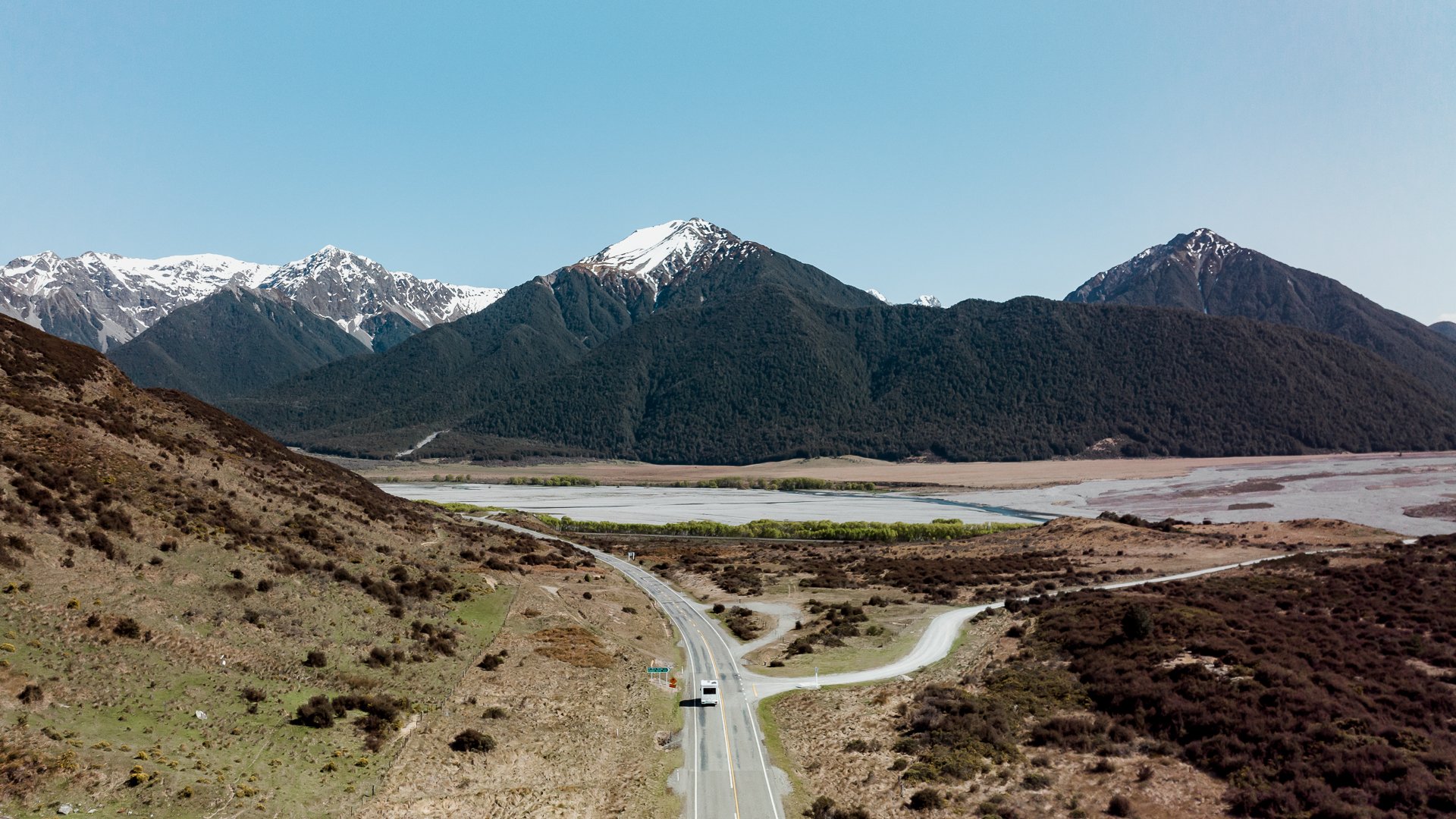 Campervan overlooking a turquoise lake and snow-capped mountains, South Island, NZ.