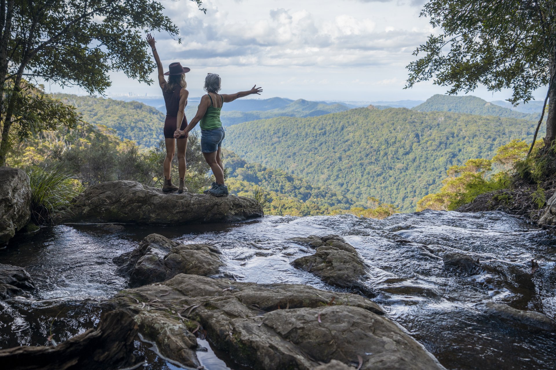 two people with their arms out, standing on top of a mountain