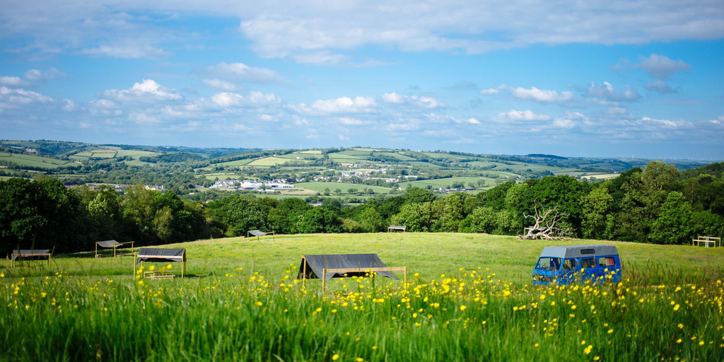 Campervan parked at picturesque, independent campsite. Rolling green hills and tents visible.