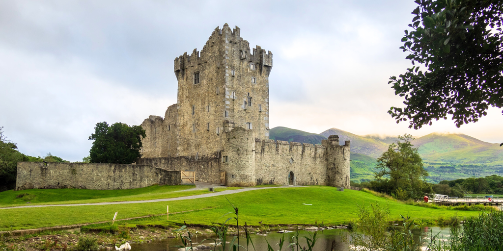 Campervan driving along a rugged Irish coastline, with green fields and the ocean visible.