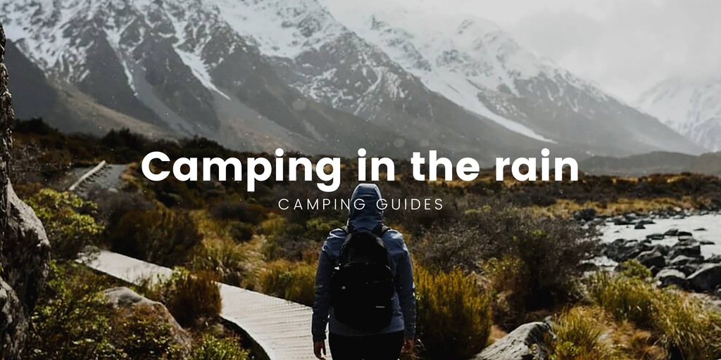 Tent pitched in a rainy forest, with a camper looking out, cuppa in hand. Wet weather camping in the bush.