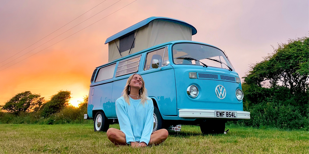 VW campervan overlooking Cornish coastline. Surfer with board walking to beach.