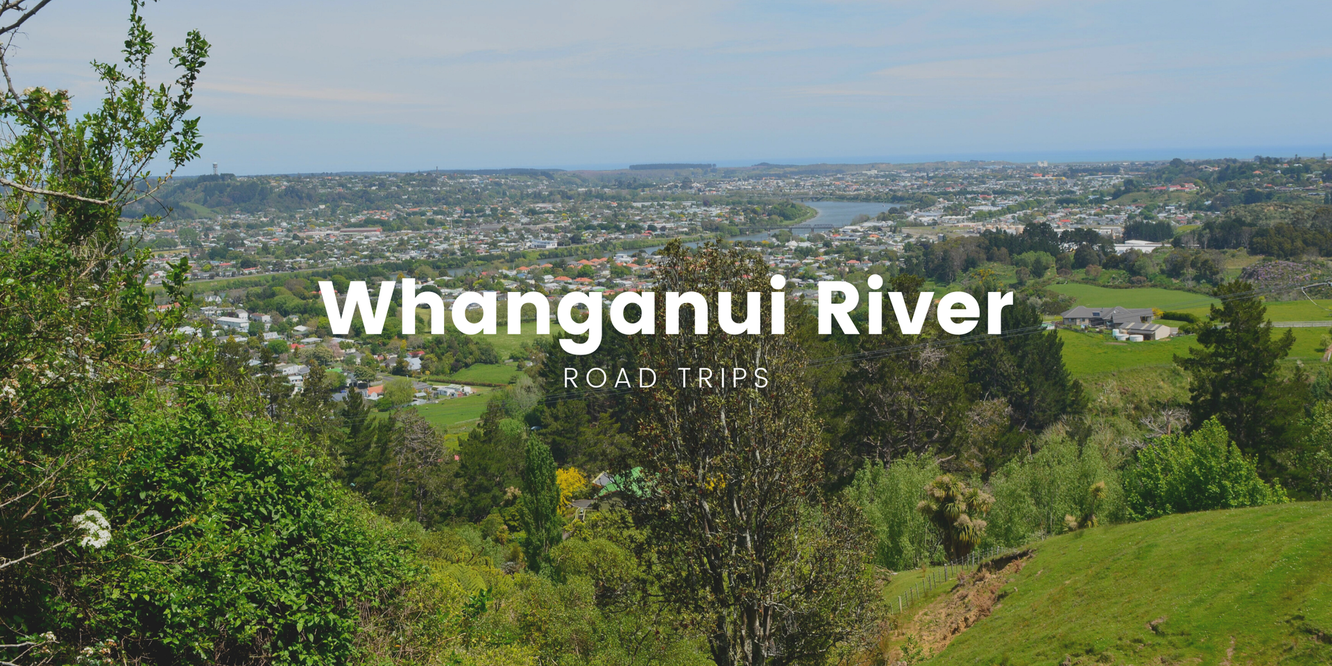 Caravan parked by the Whanganui River, lush bush in the background. Road trippin' Aotearoa!