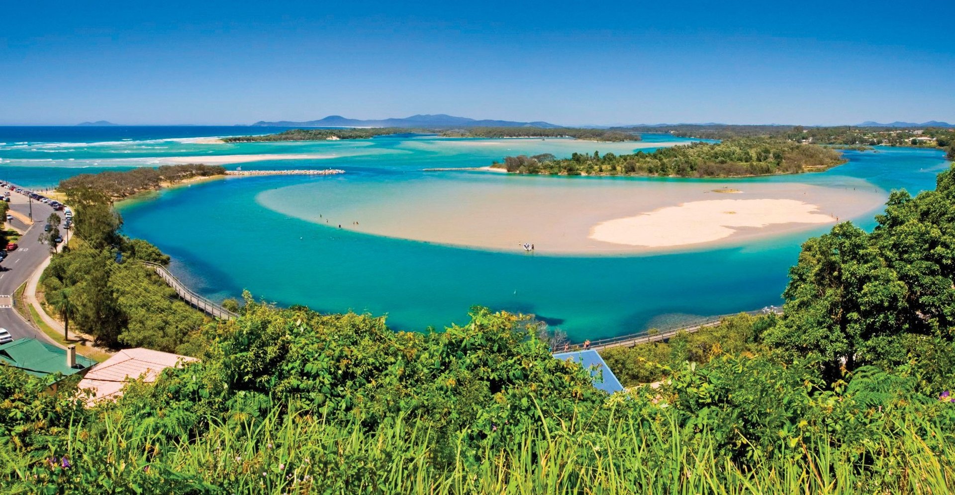 Scenic view of a coastal lagoon with turquoise water, sandy beaches, and lush greenery under a clear blue sky.