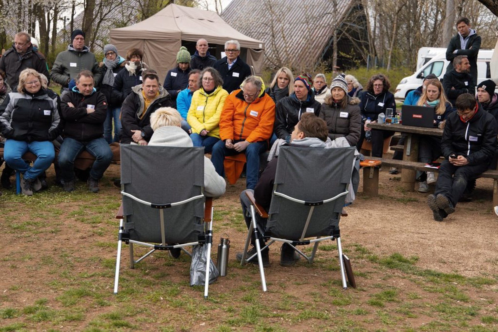 Menschen sitzen in Campingstühlen und stehen im Kreis