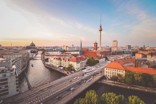 Luftaufnahme von Berlin bei Sonnenuntergang mit dem Fernsehturm, der Spree und historischen Gebäuden mit roten Dächern und baumgesäumten Straßen.