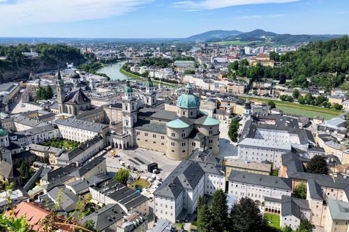 Luftaufnahme von Salzburg, Österreich, mit historischen Gebäuden, Kirchen und der Salzach, die sich durch die Stadt schlängelt, mit Hügeln im Hintergrund.