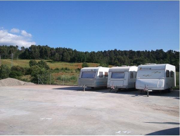 Autocaravana estacionada en parking vigilado con montañas al fondo. Almacenaje seguro en España.