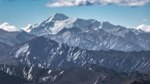 Snow-capped mountain range under a clear blue sky, with rugged peaks and scattered clouds.