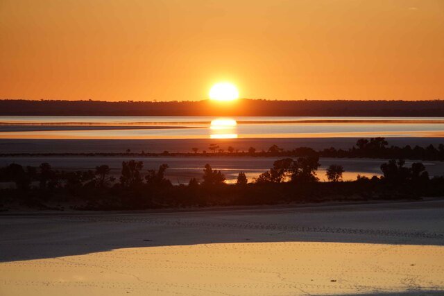 Sunset over a serene lake with a golden sky, silhouetted trees, and reflections on the water's surface.