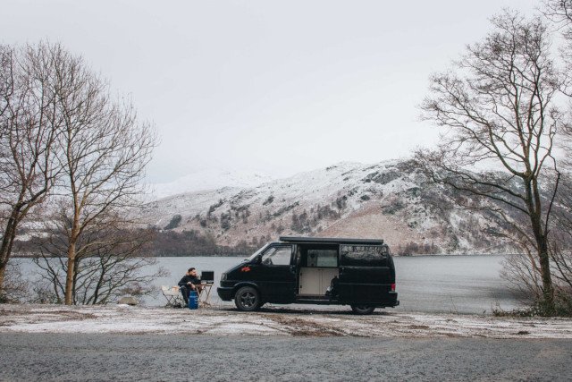 A campervan parked in the snow with a man sitting outside