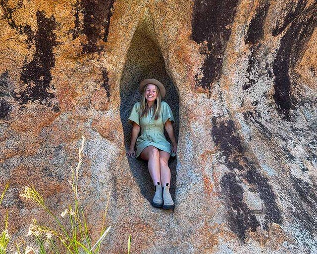 A woman sitting between the gap in a large rock