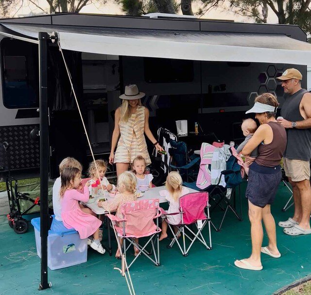 A family sitting around a camping table outside a Camplify caravan