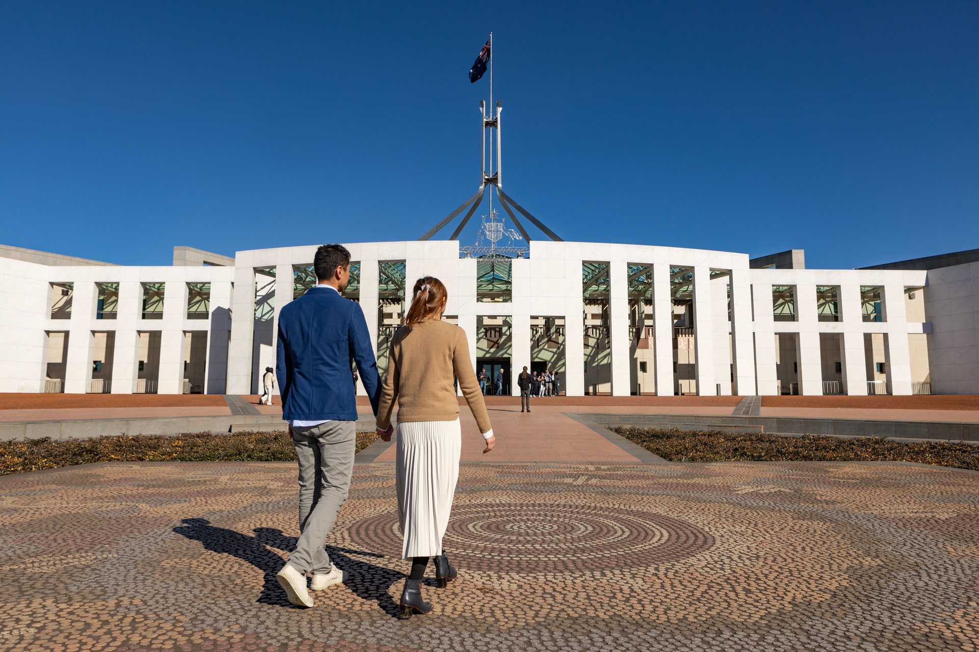A couple holding hands walking in front of a large white building