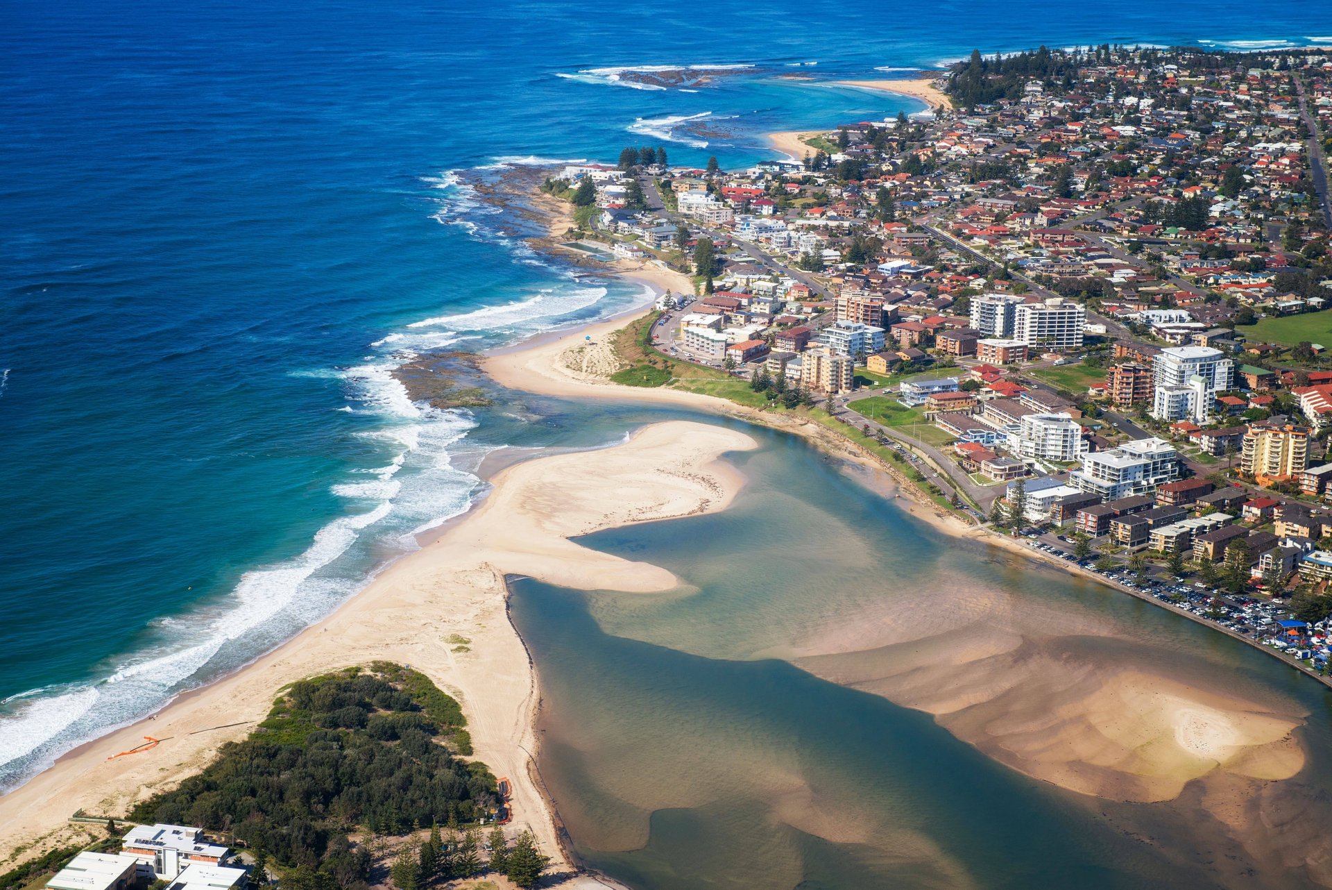 Aerial view of a coastal town with sandy sandbars, lagoon and turquoise ocean waves meeting beaches.