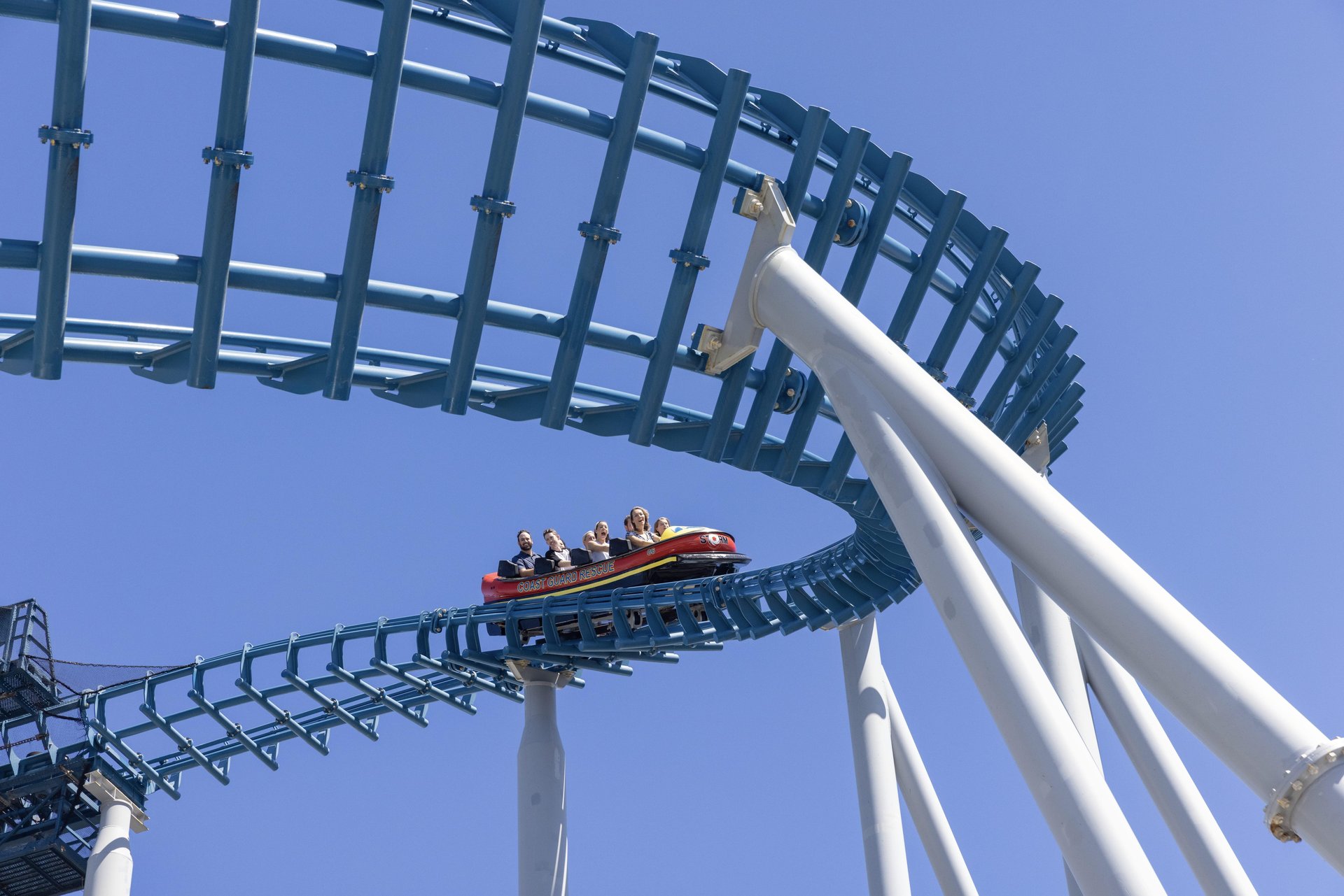Roller coaster with passengers, navigating a high blue track loop against a clear blue sky.