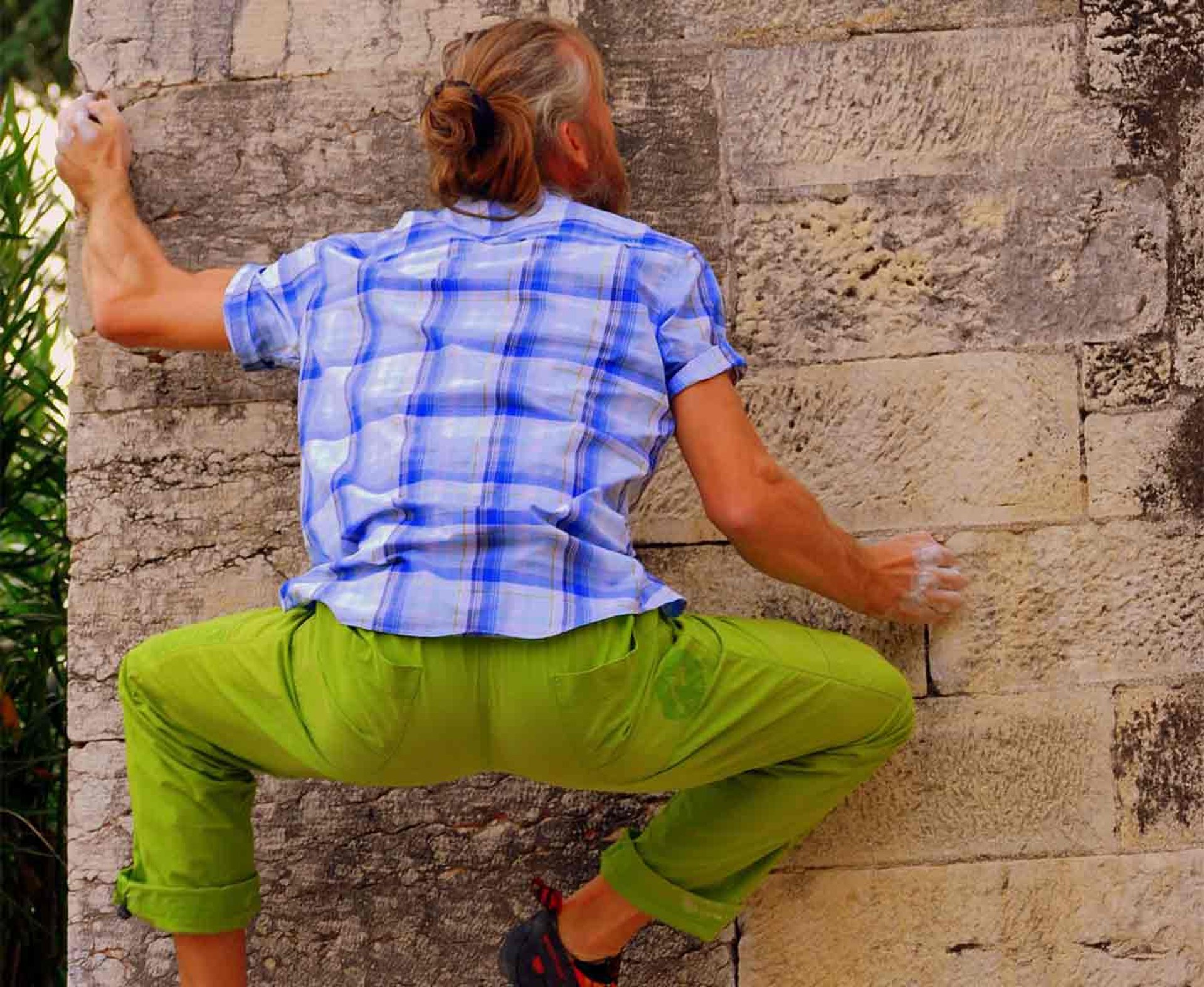 Mann in grüner Hose und kariertem Hemd klettert an einer Hauswand hoch, Bouldern mit PaulCamper